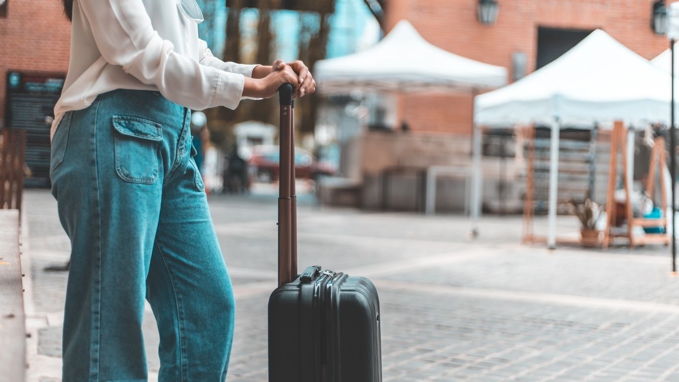 A traveller standing with a suitcase at a transport stop